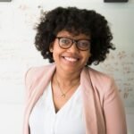 Smiling businesswoman with glasses and afro hairstyle in an office setting.